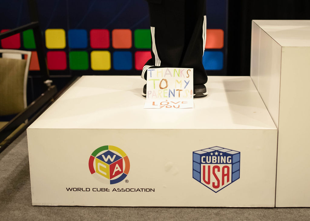 A competitor standing on a podium with a hand-written note at their feet which reads: "Thanks to my parents! Love you"
